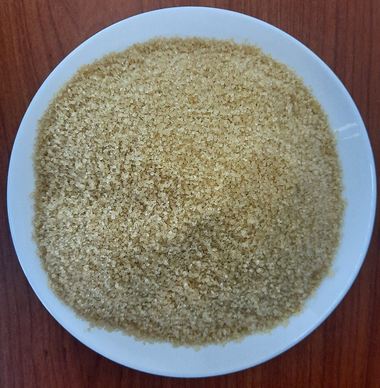A white plate filled with loose, light brown sugar crystals on a wooden table