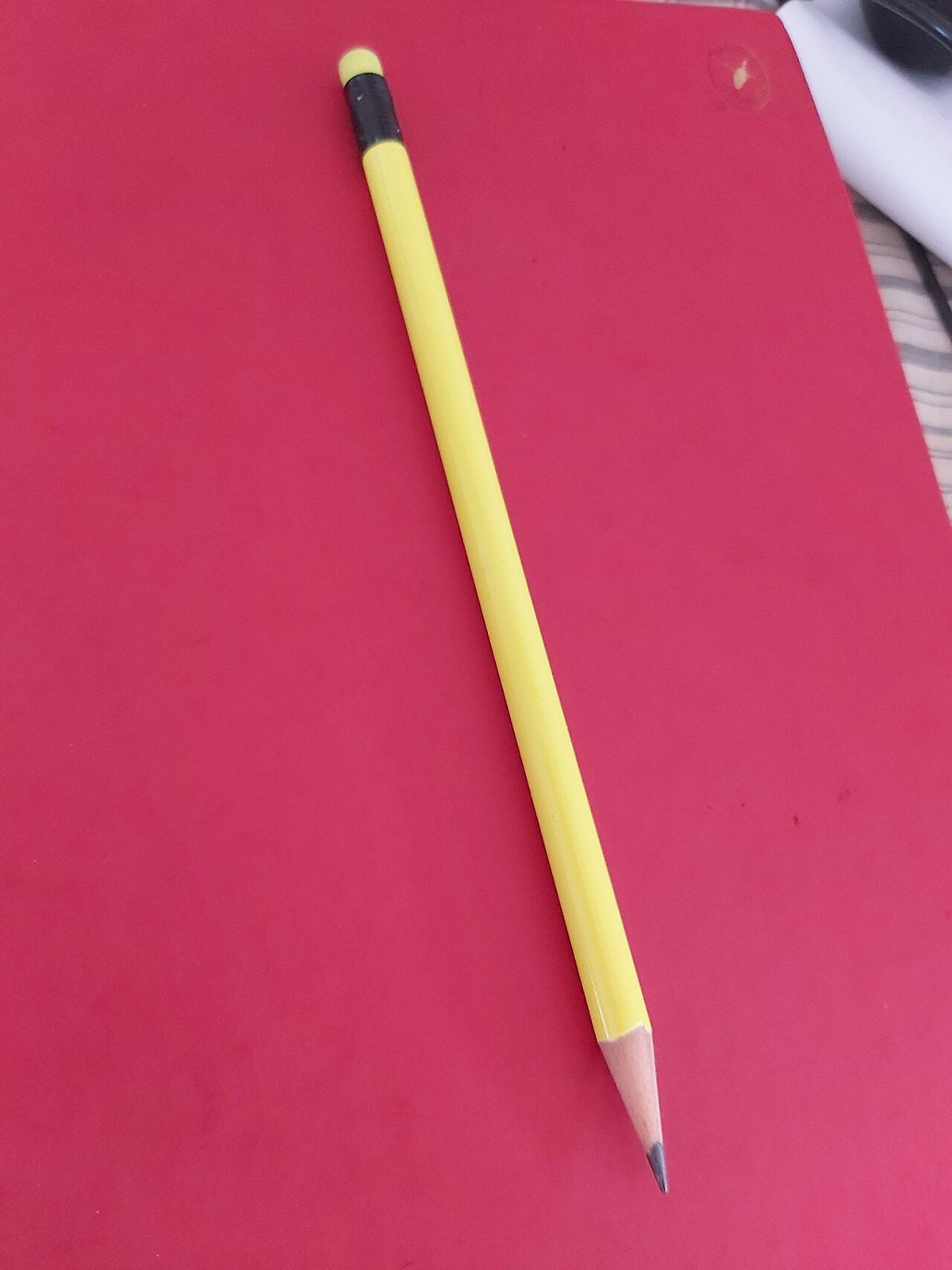 A single yellow pencil with a sharpened point, black metal band and eraser lying on a red sheet of paper